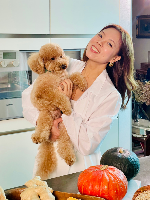 Woman holding a small brown dog in a kitchen with pumpkins on the counter.